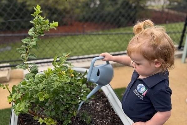 Young child watering garden plants in MKU outdoor classroom